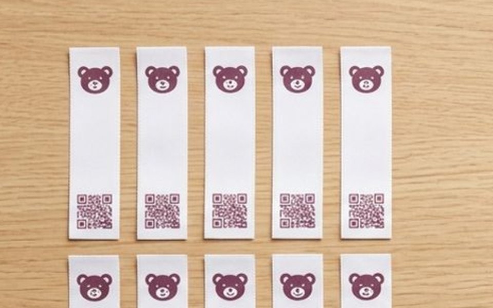 Slim white Teddy Tags iron-on labels, each with a plum teddy face and a QR code