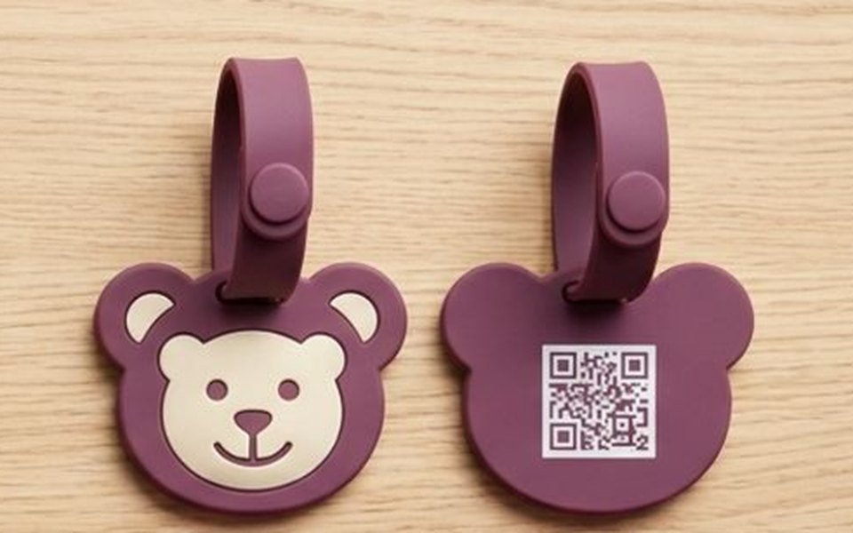 Two chunky plum teddy-shaped silicone bag tags on moulded locking loops, one showing a QR code